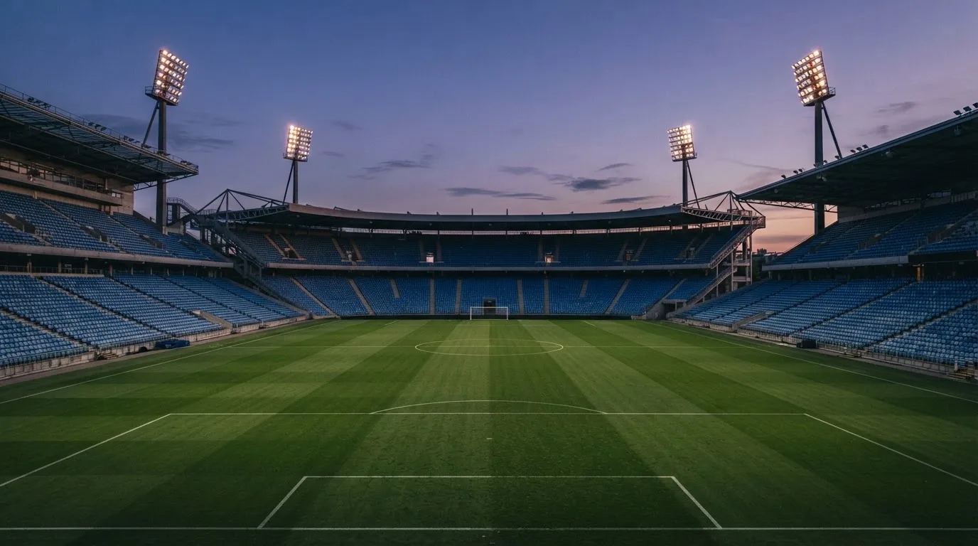 An empty football stadium with floodlight masts at dusk